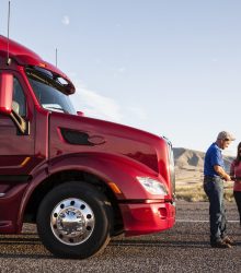 Husband and wife driving team checking their itinerary while standing in front of their commercial truck.