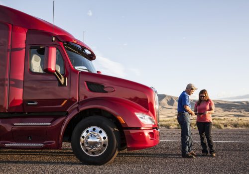 Husband and wife driving team checking their itinerary while standing in front of their commercial truck.